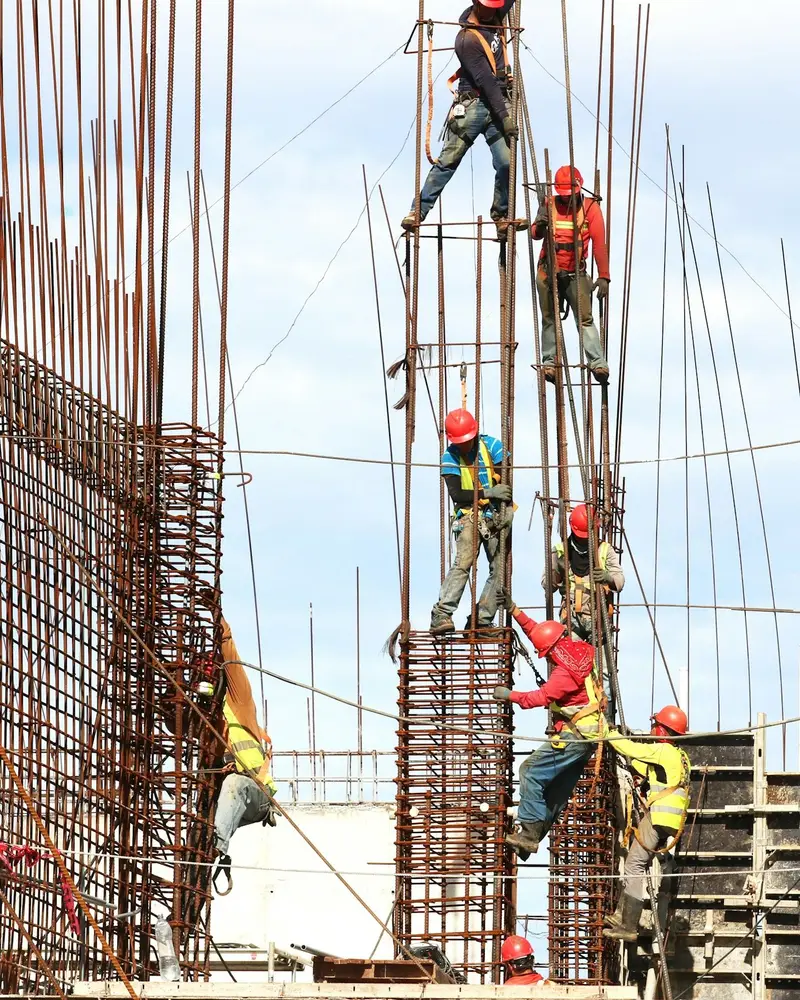 Operários de capacete e colete montando as armaduras de aço de uma obra